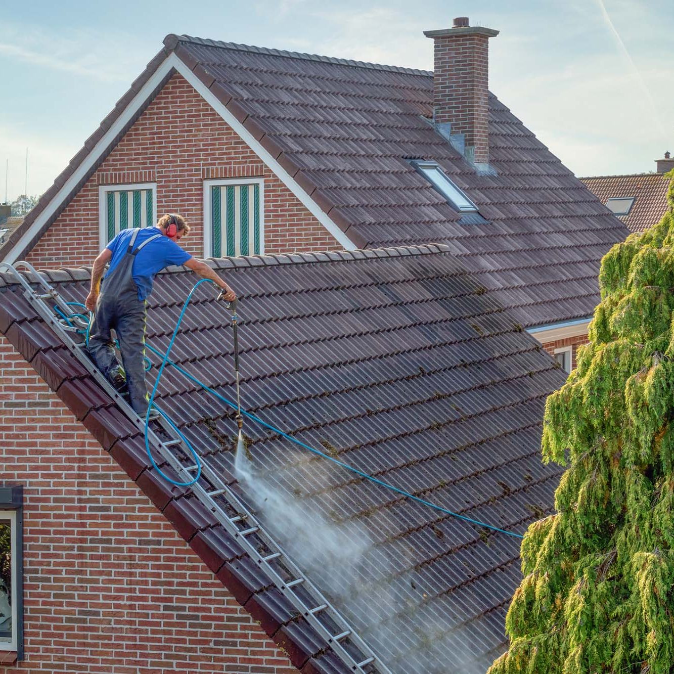 Urk, The netherlands - September 15, 2020: Cleaner with pressure washer at roof of house cleaning the roof tiles, removing moss and weed